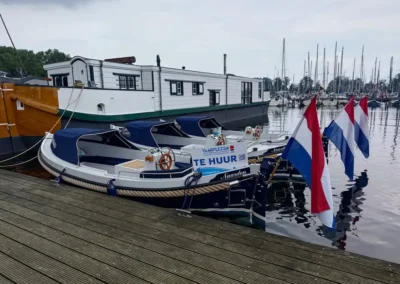 Drie blauw en witte Weco 635 sloepen van Vaarplezier Bootverhuur achter elkaar aangemeerd aan de steiger van Jachthaven Naarden